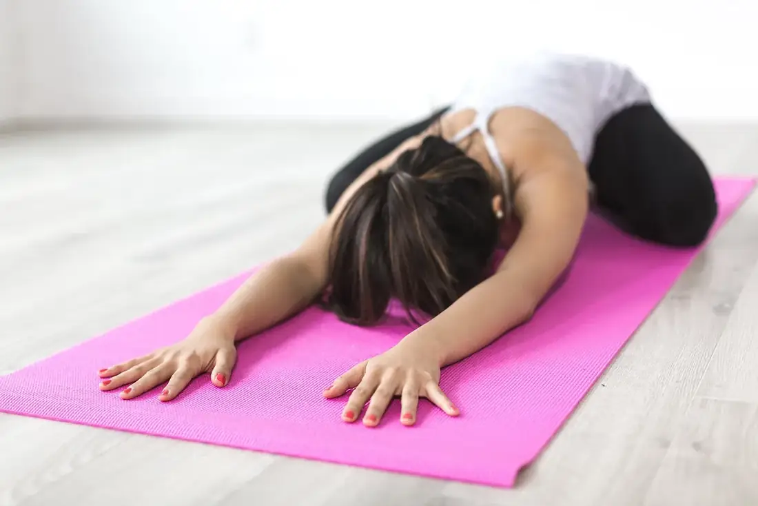 A person stretching in child's pose on a pink yoga mat