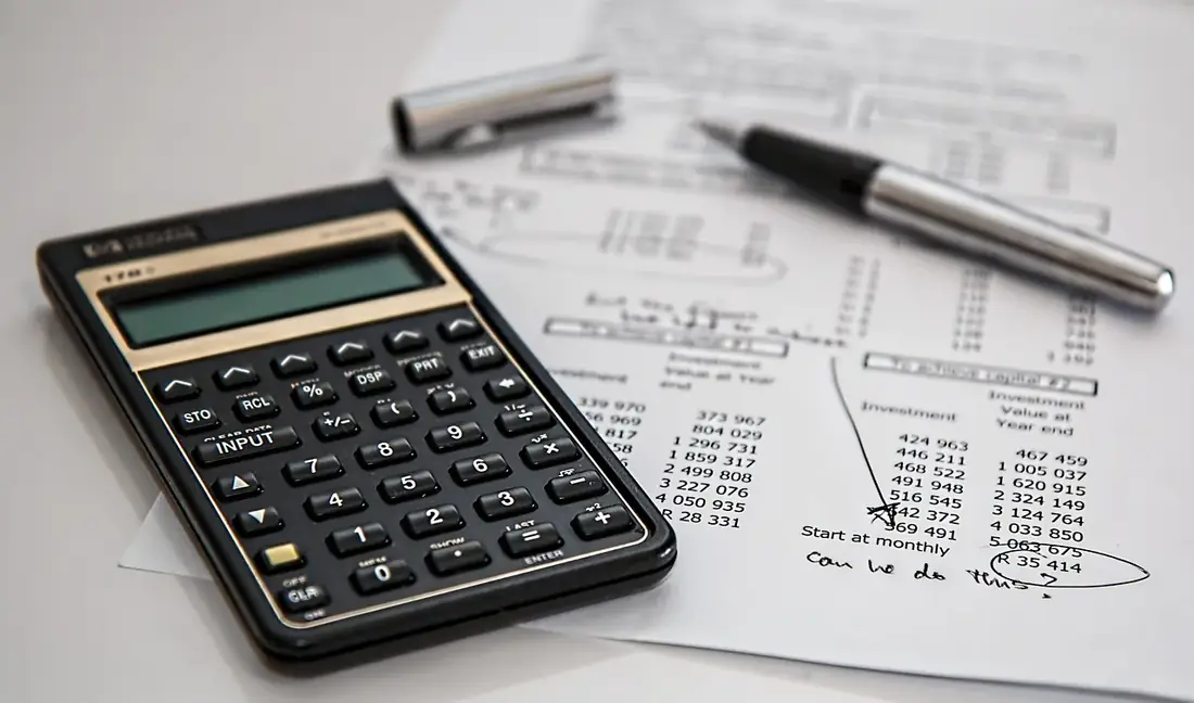 A calculator, pen and papers on a desk