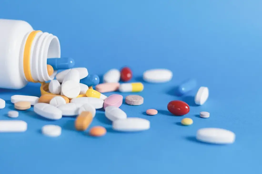 Tablets and capsules spilling from a bottle on blue